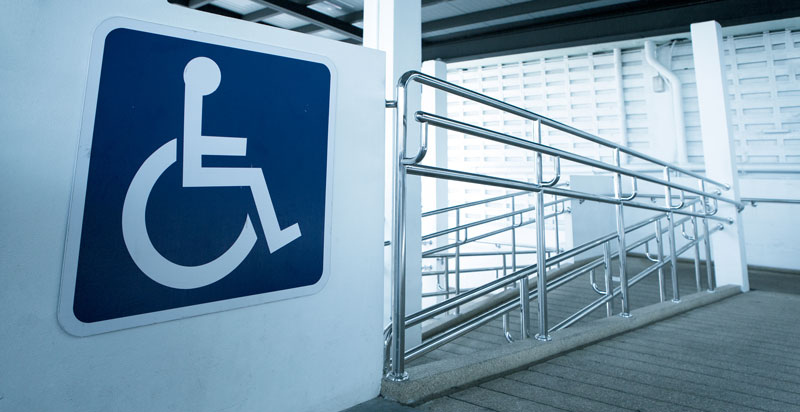 Large handicap sign at the top of a large concrete ramp in an industrial building.